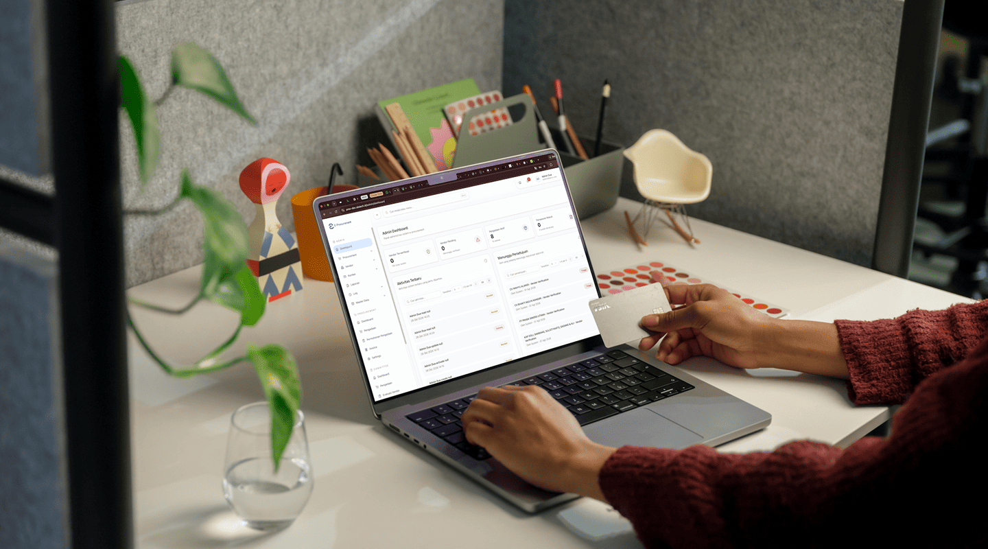 Person holding a card while using a laptop showing an E-Procurement dashboard on a bright, tidy office desk
